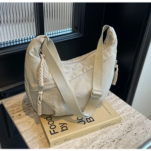 Detail of beige nylon crescent bag featuring adjustable strap and woven knot zipper pull