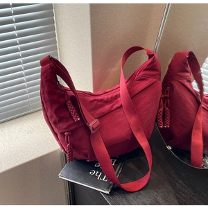 Close-up of burgundy nylon dumpling bag with adjustable strap and braided zipper pull detail