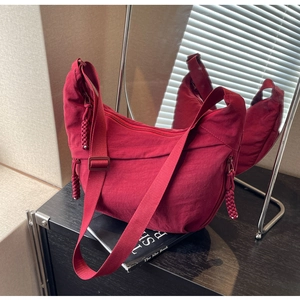 Detail view of burgundy nylon crescent bag with woven zipper pulls and pocket textures
