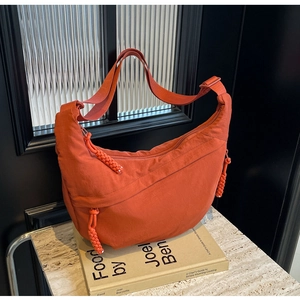 Detail of burnt orange nylon crescent bag with adjustable strap and woven zipper pulls