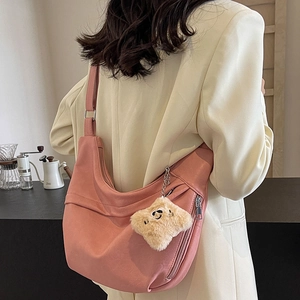 Pink crescent shoulder bag with plush bear charm worn by a model in a modern cafe setting