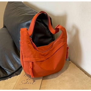 Detail of an orange nylon crescent bag featuring a unique braided zipper pull on stone texture