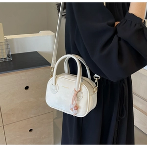 Détail d'un mini sac carré blanc crème avec deux poignées et breloque en perles roses