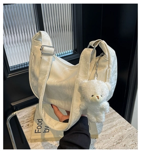 Bolso de media luna blanco con textura plisada y detalle de colgante de osito suave
