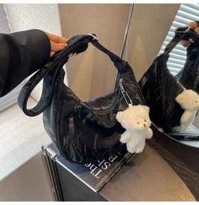 Detalle de bolso medialuna de cuero plisado negro con correa ancha y colgante de oso