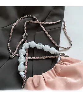 Close-up of pink velvet pleated bucket bag with pearl handle and chain strap on grey fabric