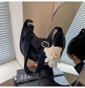 Detalle de bolso hobo plisado negro mate con colgante de oso de peluche y hebilla plata