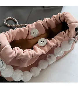 Close-up of pink ruched leather bucket bag with silver magnetic snap and white pearl strap