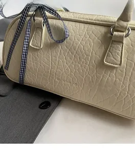 Detail of off-white Boston bag featuring pleated leather texture and a blue ribbon bow