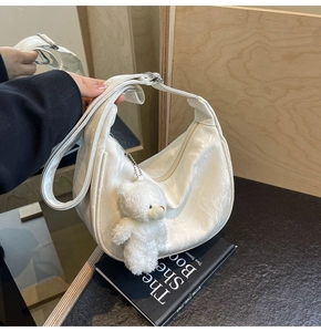 Detalle del bolso hobo blanco con textura plisada y colgante de osito de peluche