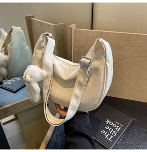 Detalle de un bolso de media luna blanco roto texturizado con un lindo amuleto de oso.