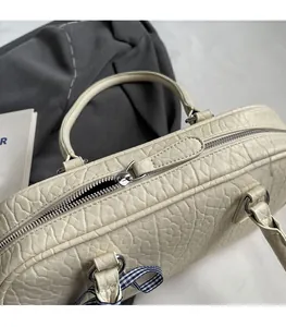 Close-up of smooth silver metal zipper and plaid bow on cream textured underarm bag