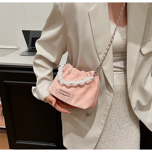 Detail of pink velvet bucket bag with white pearl handle and chain strap on a model