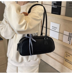 Close-up of black textured leather cylinder bag with ribbon detail and silver hardware
