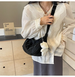 Detalle del bolso hobo plisado negro con charm de oso de peluche blanco y correa ajustable