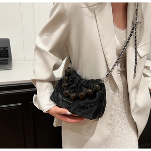 Close-up of black satin cloud bucket bag with pearl handle and metal chain strap