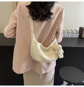 Detalle del bolso medialuna beige con textura plisada y colgante de osito de peluche