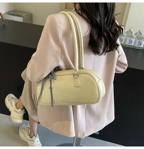 Detail of beige pleated shoulder bag featuring a blue plaid bow charm and twin straps