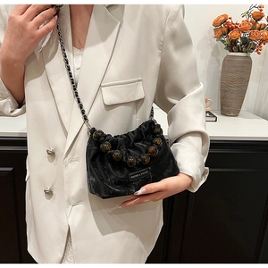 Detail of black pleated bucket bag featuring large amber beads and chain strap