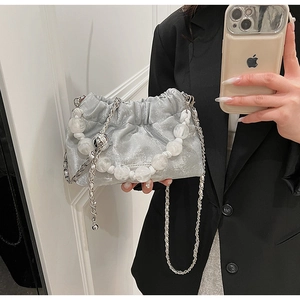Detail of silver pleated bucket bag with pearl handle and metal chain strap held by model