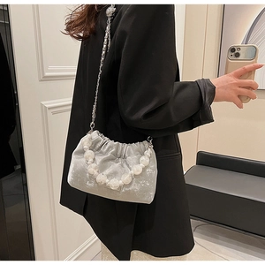 Close-up of velvet pleated bucket bag with pearl handle and metal chain on a model