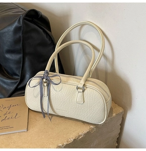 Detailed view of cream cylinder bag with leather texture and blue checkered ribbon detail