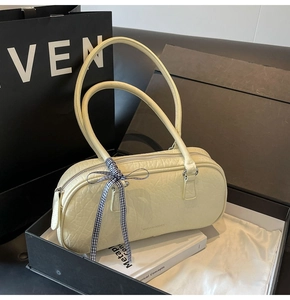 Macro detail of creamy yellow gathered leather shoulder bag with checkered bow accent