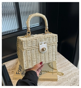 Detail view of woven straw box bag with leather buckle and gold chain strap