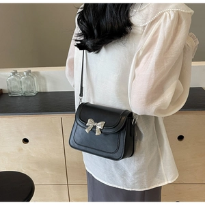 Detail van zwarte matte crossbodytas met zilveren metalen strik en slanke schouderband