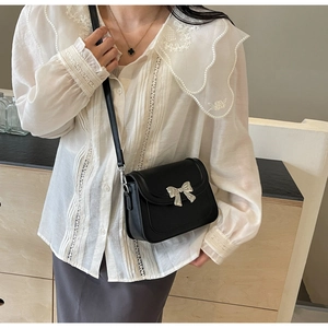Detailopname van zwarte leren crossbodytas met een decoratieve zilveren strikgesp