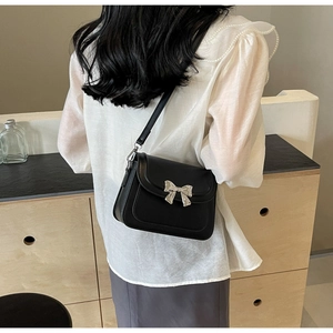 Model draagt een zwarte crossbodytas met zilveren metalen strik en matte lederen textuur