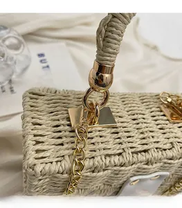 Close-up of beige woven straw bag featuring gold chain and polished metal lock detail