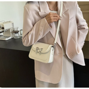 Detail van de stijlvolle zilveren metalen strik op een beige glanzende leren crossbodytas