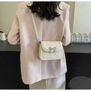 Crème crossbodytas met zilveren strikgesp gedragen door model in roze blazer