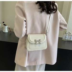 Detail van een beige lederen crossbodytas met een decoratieve zilveren metalen strik