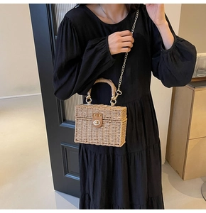 Detail of a woven straw handbag with a metal twist lock and gold chain strap
