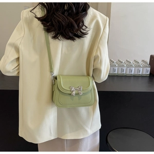 Detail van een lichtgroene crossbodytas met zilveren strik op een ivoren blazerjasje