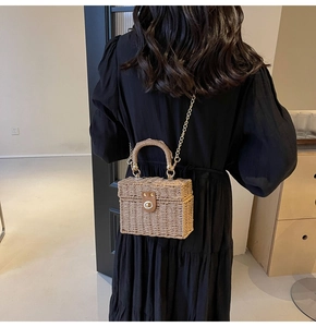Detail of a woven straw box bag with a golden chain strap and leather clasp detail