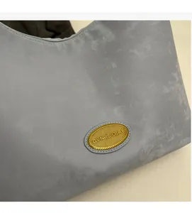 Détail du cabas gris montrant le logo ovale doré et la fermeture éclair élégante