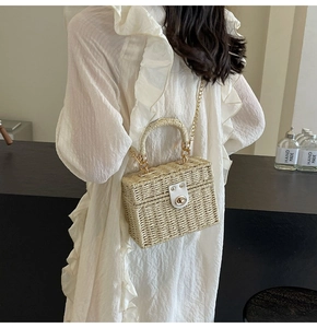 Detail of woven straw bag showing golden chain strap and white leather clasp detail