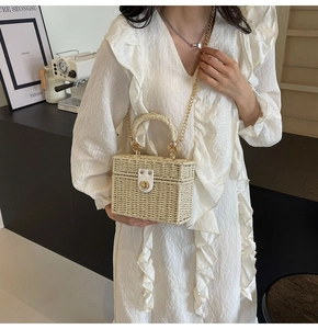 Detail of cream straw box bag with golden twist lock and chain strap on model