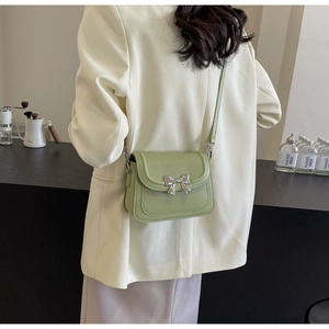 Detail van de pistachegroene crossbodytas met zilveren strikgesp op het model