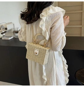Detailed view of handmade straw box bag with leather buckle and gold chain strap