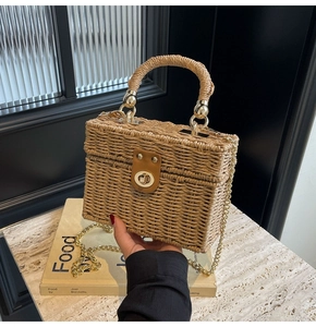 Detailed view of woven straw box bag with gold swivel lock and metallic chain strap