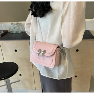 Detail van een lichtroze crossbody tas met zilveren metalen strik en een lederen riem
