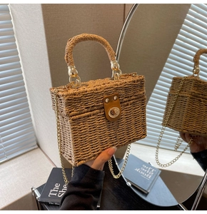 Detail of hand-woven straw box bag with golden rotary lock and chain shoulder strap