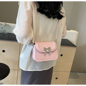 Detail van roze crossbodytas met een grote zilveren metalen strik op houten decor