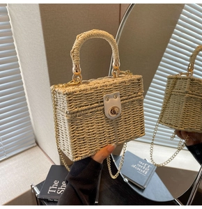 Close-up of rectangular straw handbag featuring white leather clasp and golden chain strap
