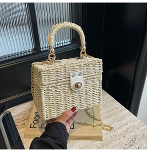 Detail of woven straw box bag with golden chain strap and white leather buckle closure