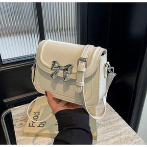 Detail van een crèmewitte crossbodytas met zilveren metalen strik en verfijnd stiksel